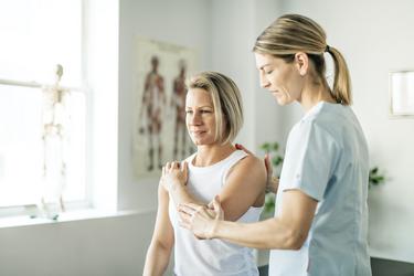 Patientin in der Reha mit Physiotherapeutin beim Ausführen von Schulterübung